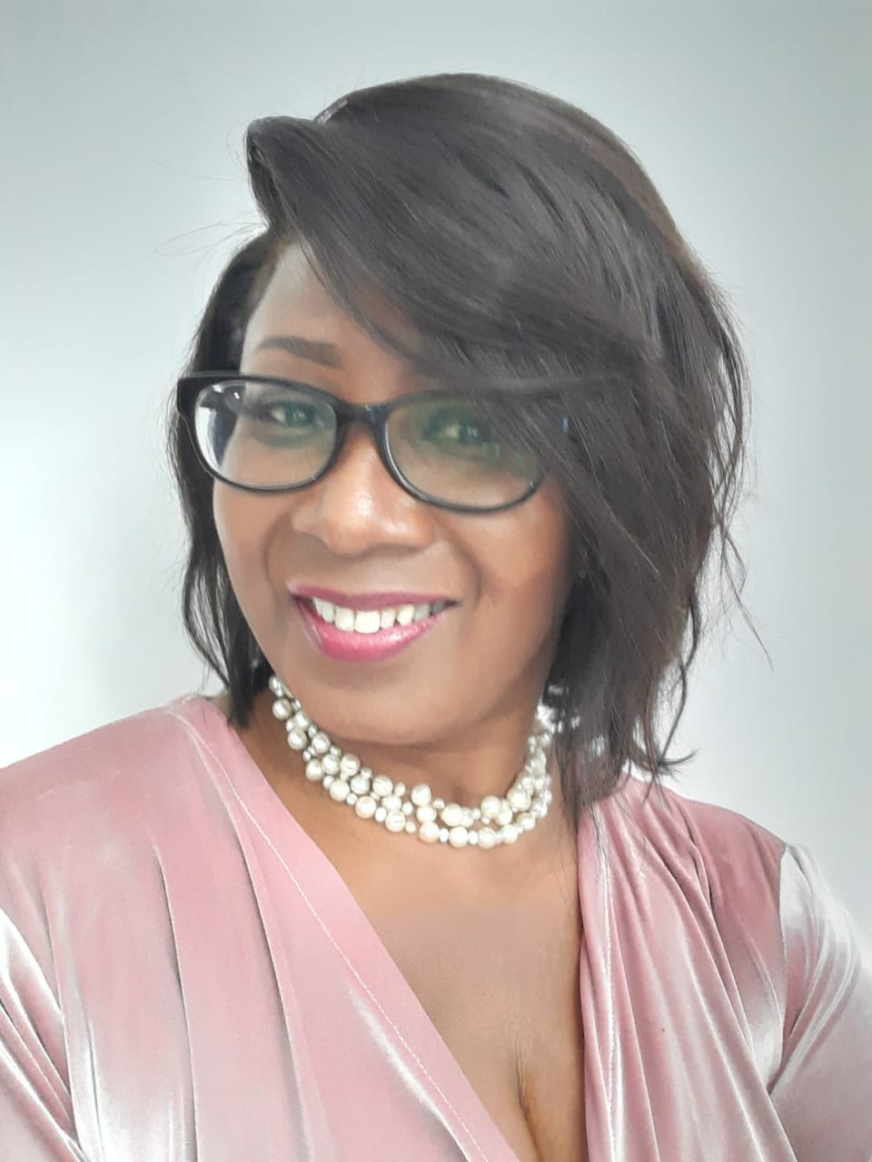 Helen Tucker, award-winning women's mentor and confidence coach, smiling warmly in a pink velvet top with a pearl necklace and glasses